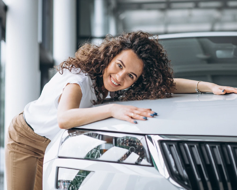 Mujer sonriente apoyada sobre su automóvil, reflejando confianza y respaldo ante imprevistos con su seguro de auto.